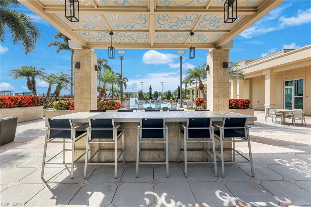 Outdoor entertainment area featuring a stone-clad bar with seating for five, a decorative overhead pergola with pendant lighting, and a patterned paver patio