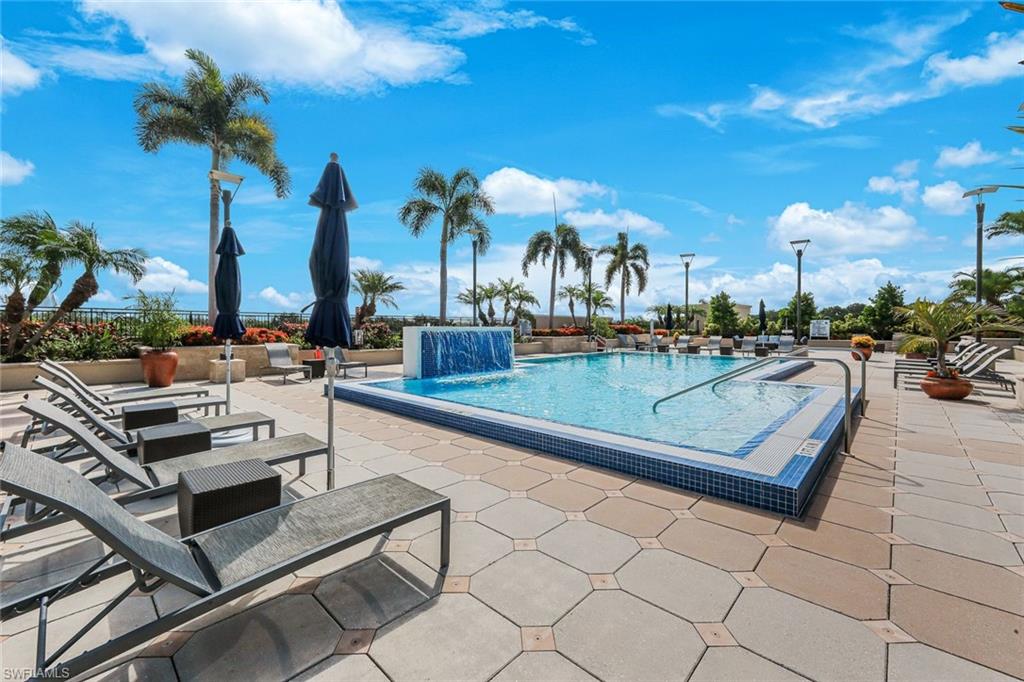 Outdoor pool deck featuring a geometric paver patio, a rectangular swimming pool with a mosaic tile border, and a built-in water feature
