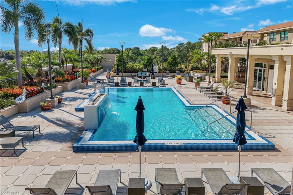 Resort-style outdoor pool area featuring a rectangular pool with a waterfall edge, surrounded by a paver patio