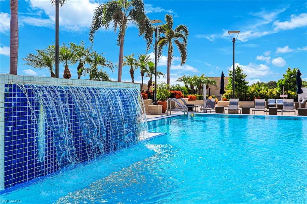 Swimming pool featuring a tiled waterfall, integrated lounging area, and surrounding palm trees