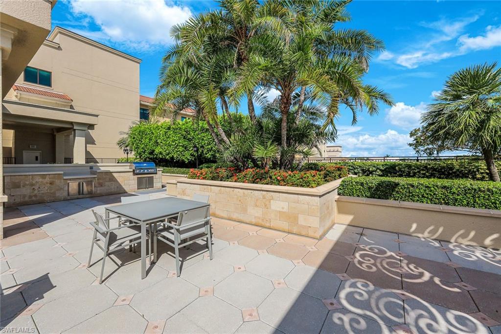 Outdoor patio featuring large format pavers with decorative inserts, a built-in grill station, stone-clad planter boxes with established palm trees, and manicured hedges