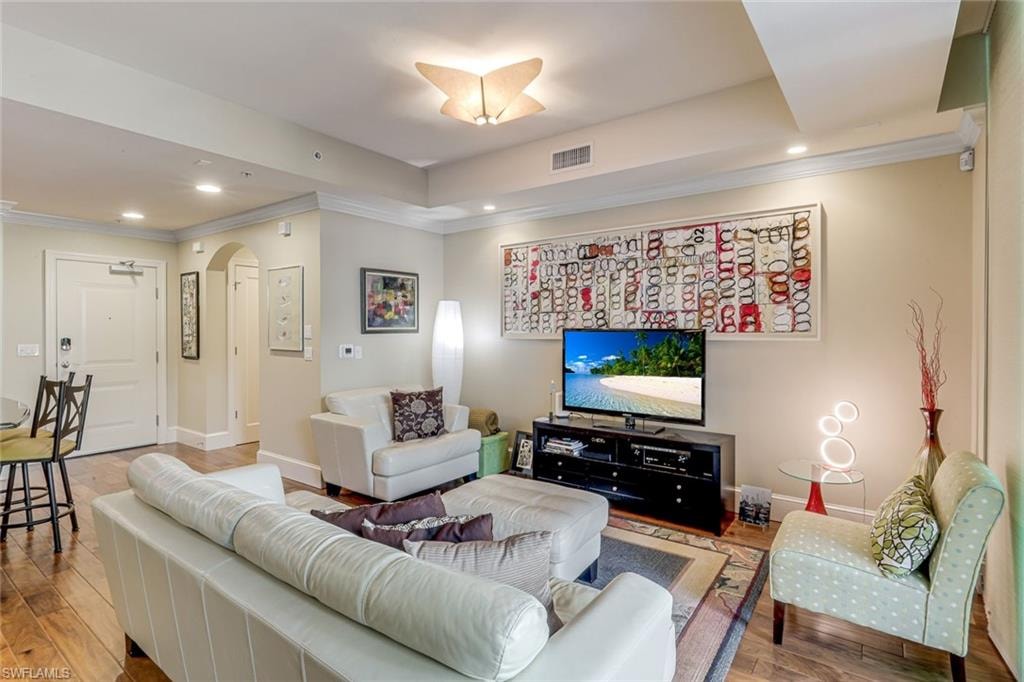 Spacious living area featuring wood-finish flooring, crown molding, recessed lighting, an arched doorway, and tray ceiling details