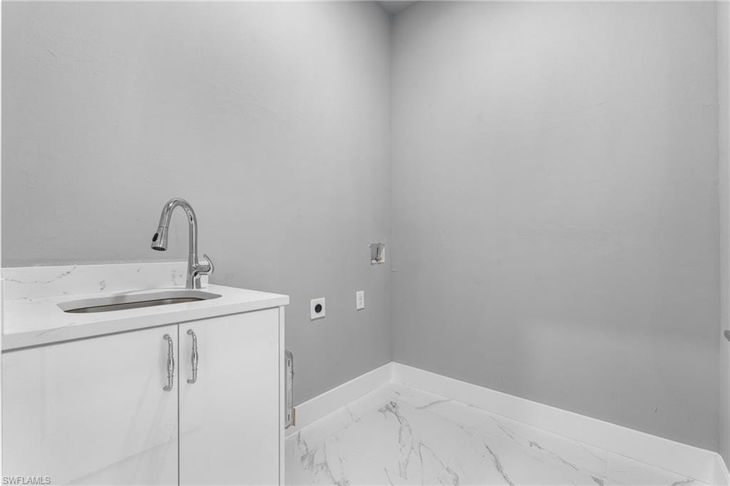 Laundry space featuring a white vanity with an integrated sink, polished chrome faucet, and a stone-finish countertop