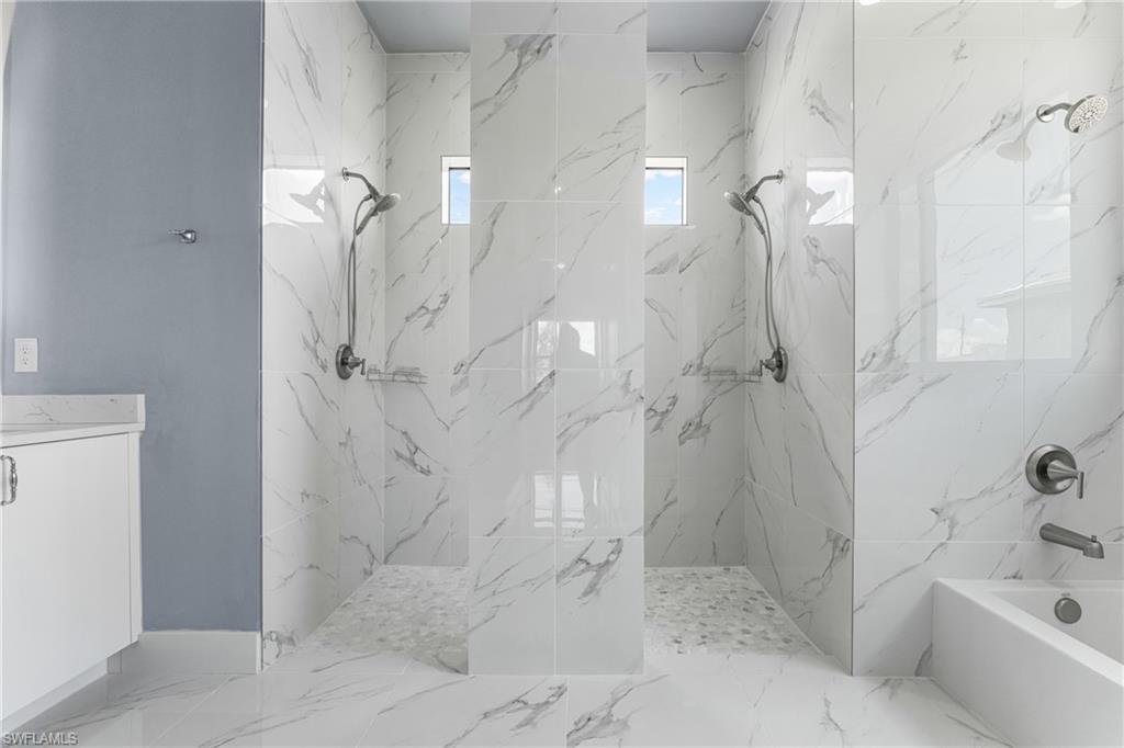 Spacious bathroom featuring two walk-in showers with tile surrounds, a separate bathtub, and a vanity with a countertop