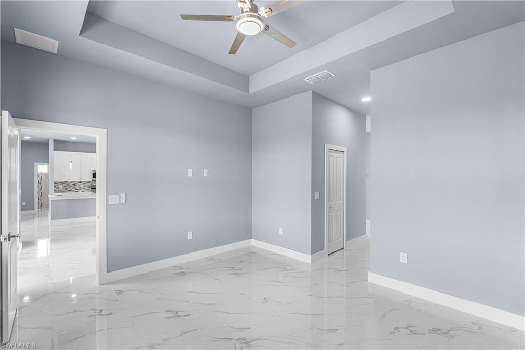 Spacious interior room featuring a tray ceiling with a ceiling fan, white baseboards, and large format polished tile flooring