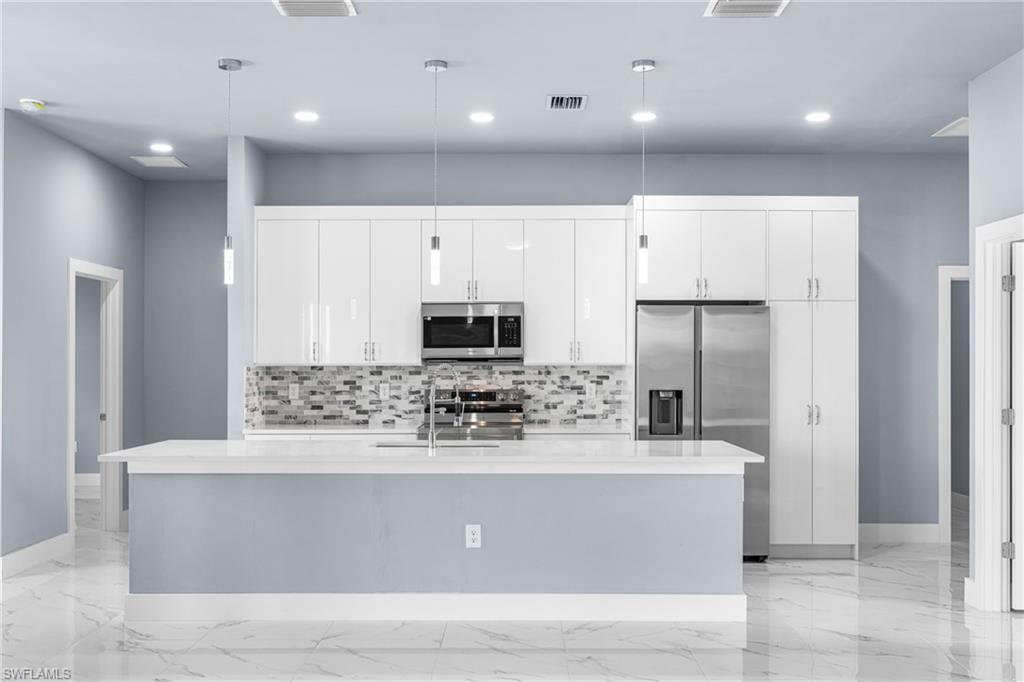 Modern kitchen featuring white high-gloss cabinetry, a stainless steel appliance suite, and a large central island with a solid surface countertop