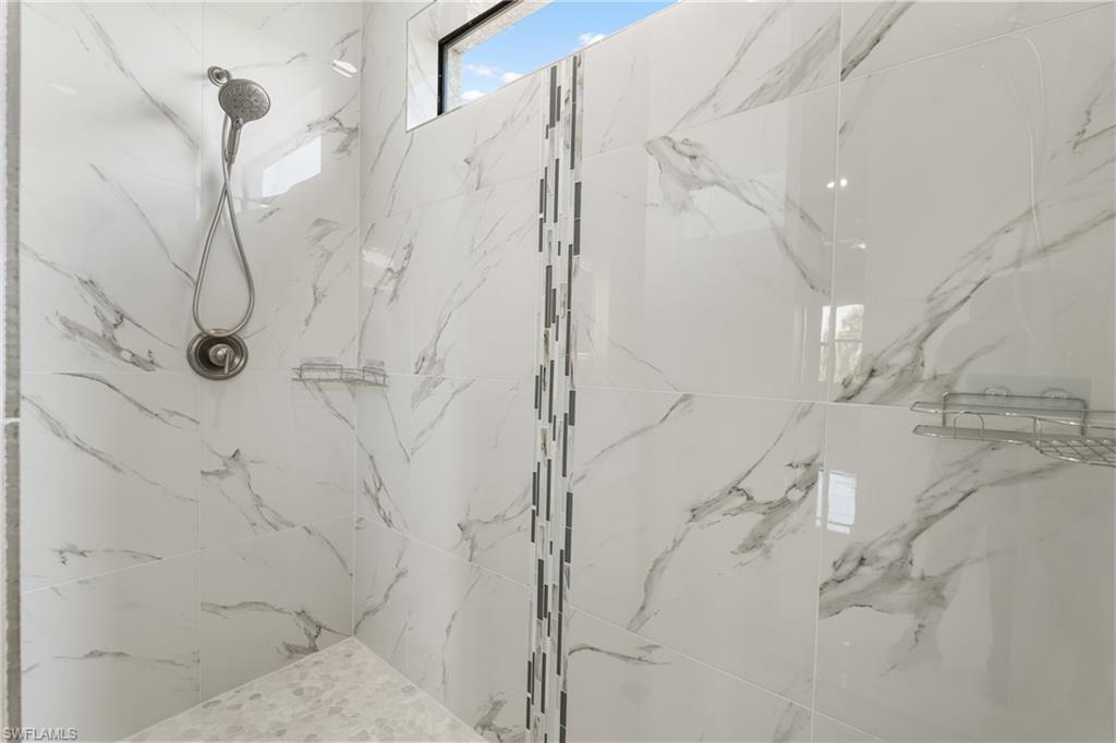 Shower featuring large format white tile with grey veining, a vertical mosaic accent strip, and a handheld shower head with brushed nickel finish
