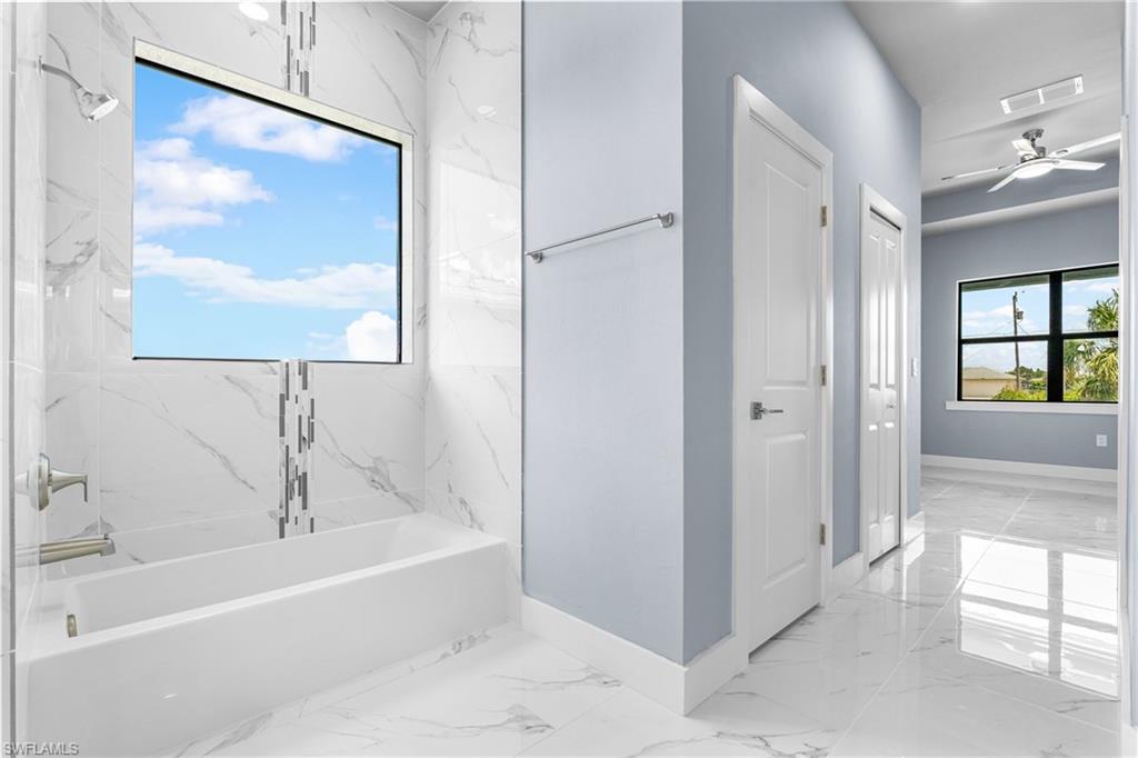 Bathtub with a large window, surrounded by white marble-look tile walls featuring a decorative vertical accent