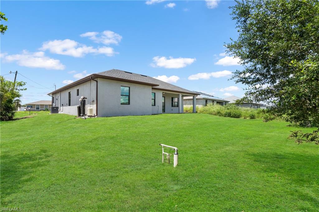 Expansive green lawn surrounds the property, featuring a stucco exterior with a covered patio