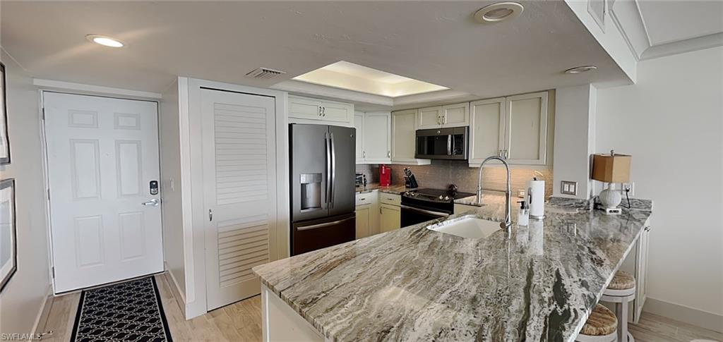 Modern kitchen featuring a large island with a substantial stone countertop, an undermount stainless steel sink with a high-arc faucet, white shaker-style cabinetry, and stainless steel appliances