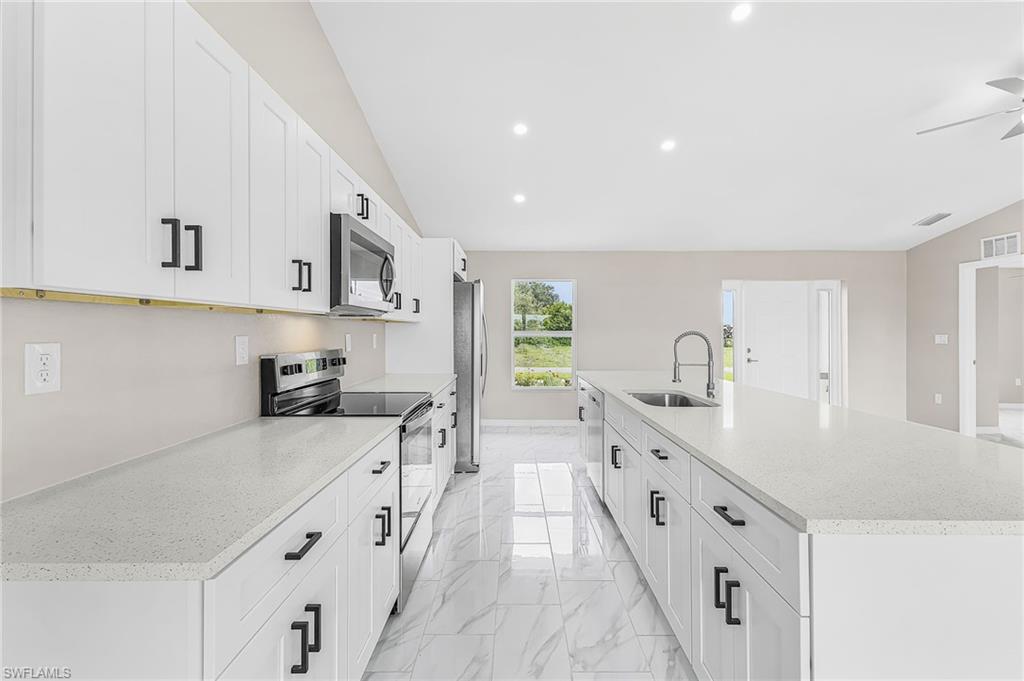 Contemporary kitchen featuring an expansive island with a stainless steel sink, white shaker cabinetry with black hardware, white countertops, and a full suite of stainless steel appliances