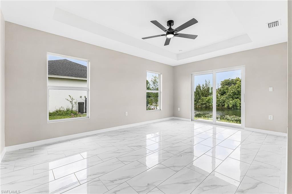 Spacious room featuring white rectangular tile flooring, a tray ceiling, and a ceiling fan with a matte black finish