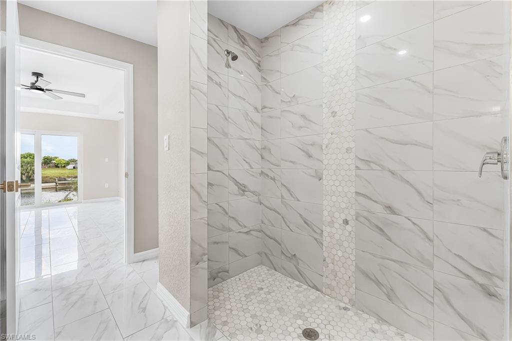 Spacious walk-in shower featuring large format marbled tile walls, a decorative vertical accent strip of hexagonal tiles, and a coordinating hexagonal tile floor