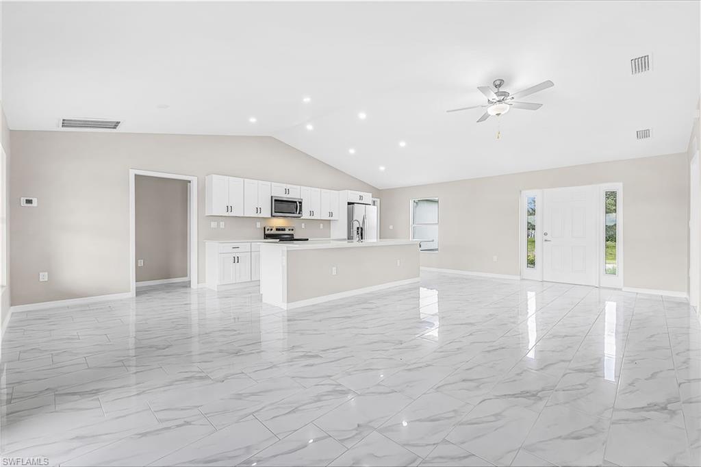 Open-concept living space featuring a vaulted ceiling with recessed lighting, tile flooring, and a kitchen island with a sink