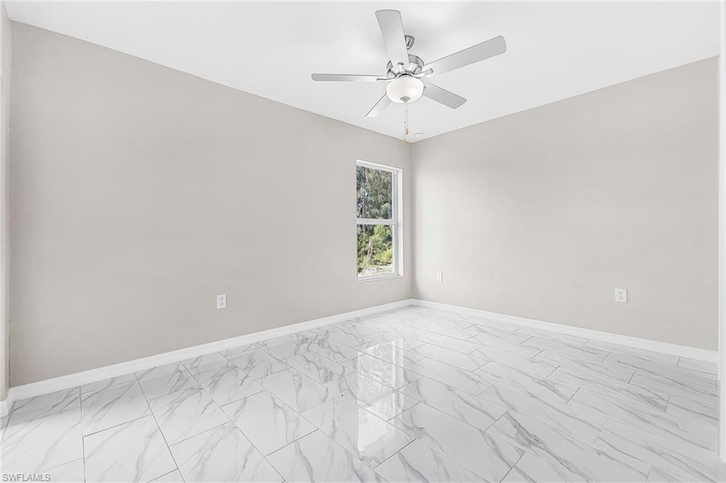 Spacious interior room featuring large format tile flooring, a single window, and a ceiling fan with integrated lighting