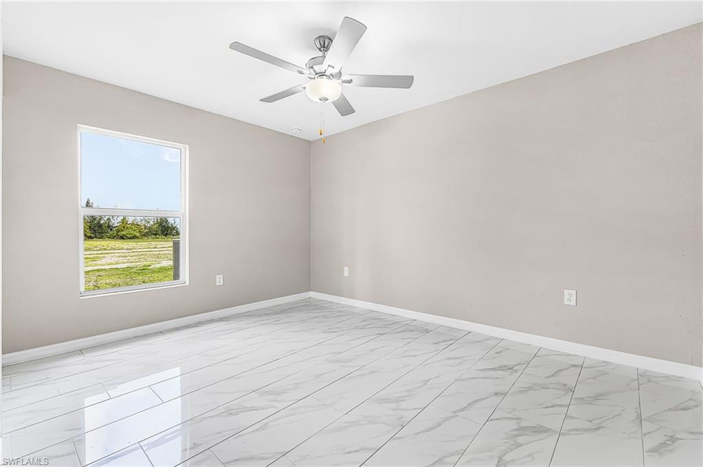 Spacious room featuring large format tile flooring, a window offering exterior views, light gray wall paint, white baseboards, and a ceiling fan with integrated lighting