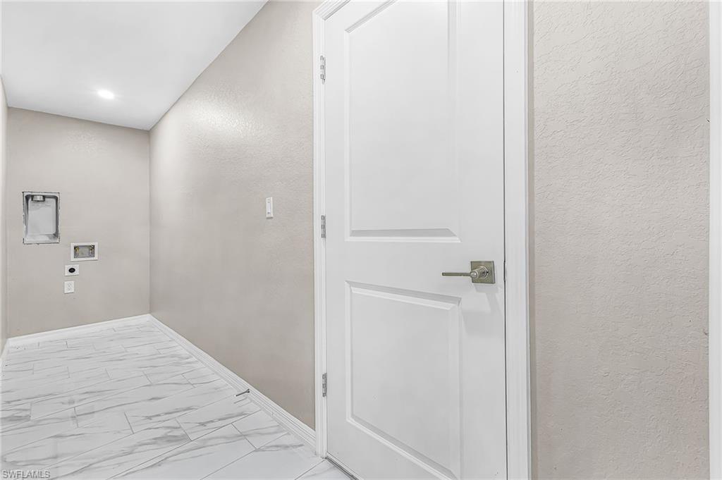 Utility room featuring white tile flooring with gray veining, light gray textured walls, and a white interior door with brushed nickel hardware