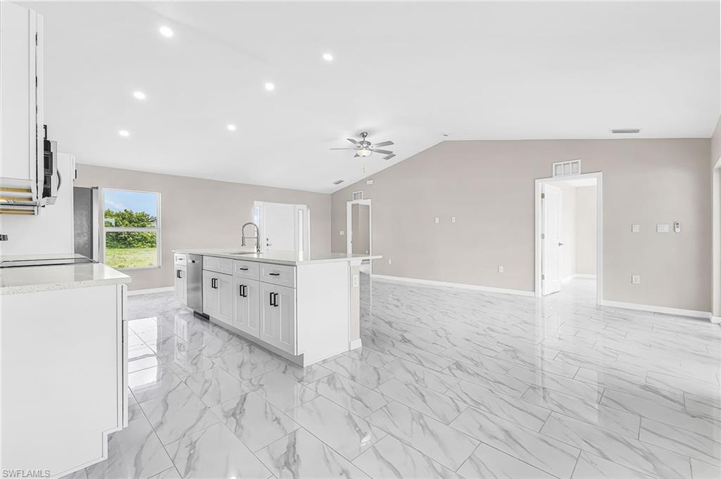 Spacious open-concept living area featuring large format marble-look tile flooring, a vaulted ceiling with a ceiling fan, and recessed lighting