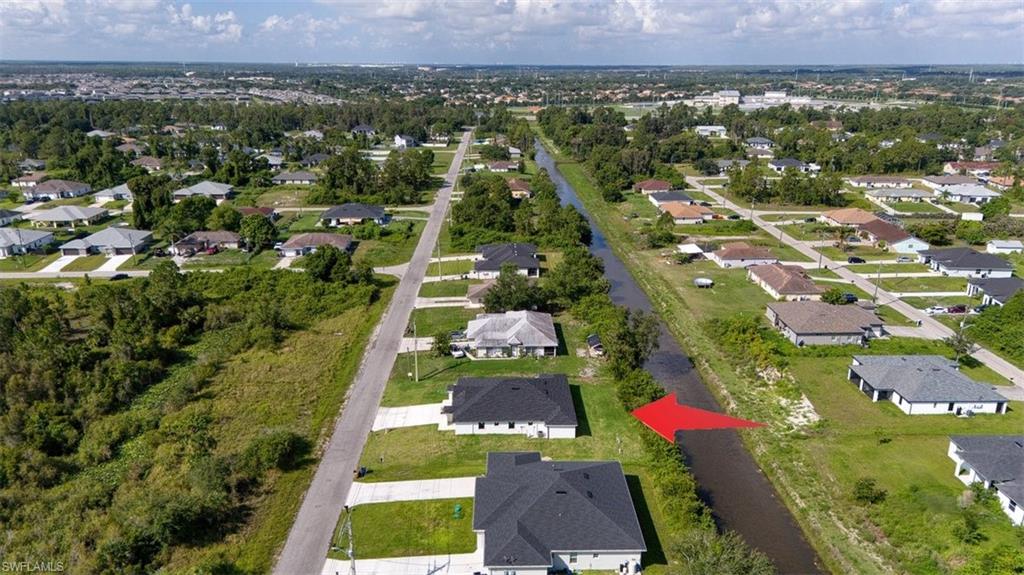 Canal-front property featuring a developed residential street, surrounding green spaces, and a distant urban landscape