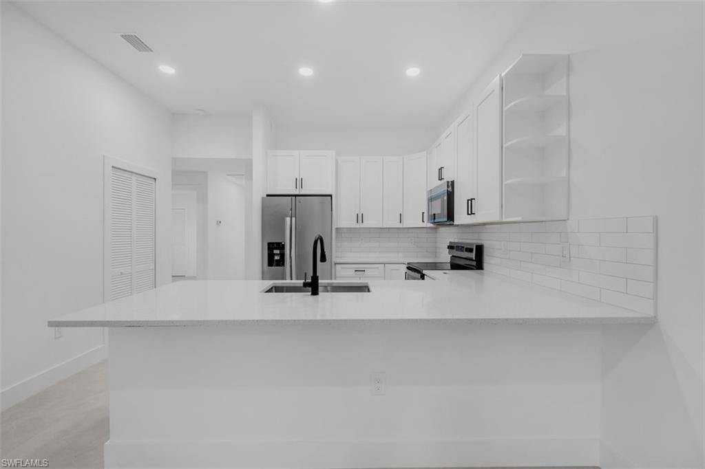 Modern kitchen featuring a large white countertop island, stainless steel appliances, white cabinetry with black hardware, a subway tile backsplash, and recessed lighting