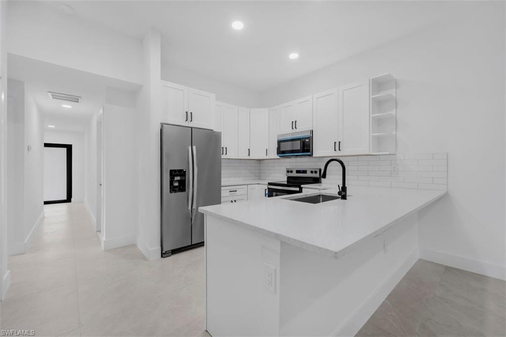 Modern kitchen featuring white shaker cabinetry, stainless steel appliances, white subway tile backsplash, and a large island with a black sink and faucet
