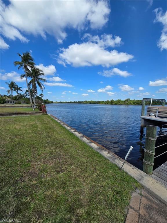 Waterfront property featuring a private dock, lush green lawn, mature palm trees, and direct water access
