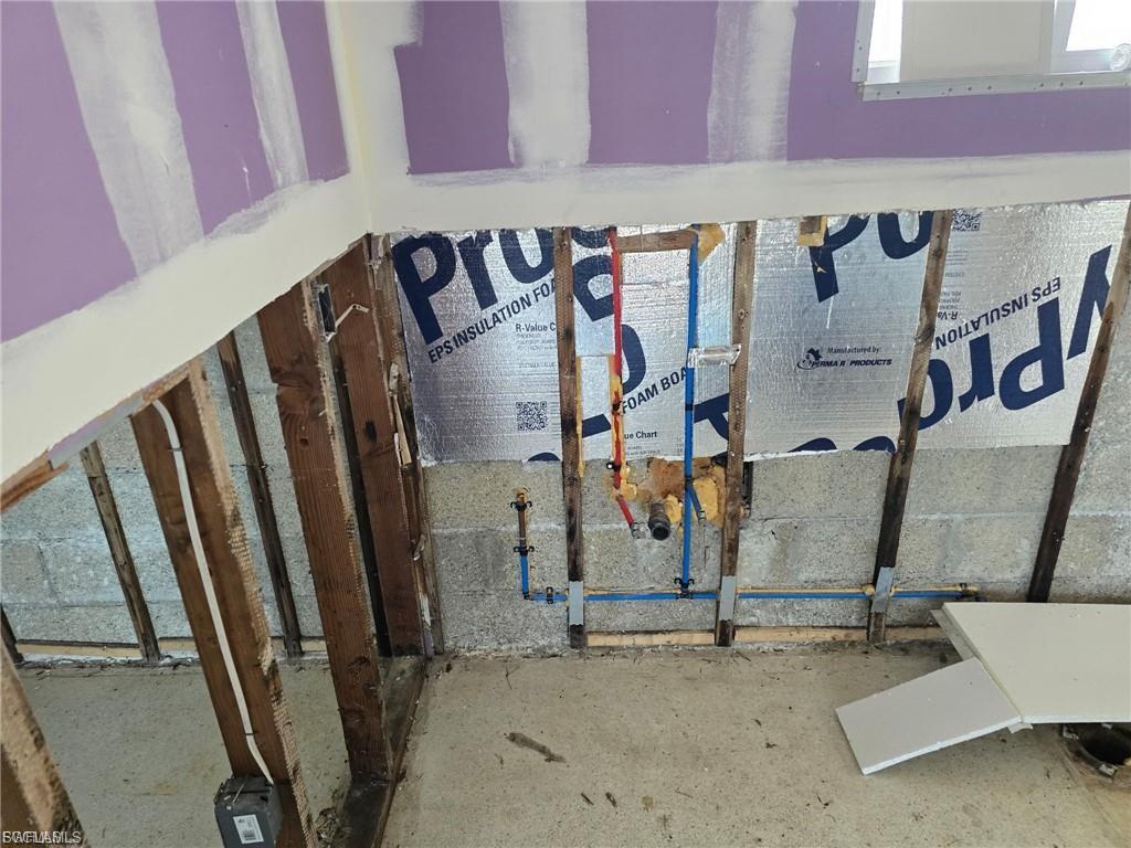 Framed wall with visible plumbing lines, insulation, and concrete block foundation