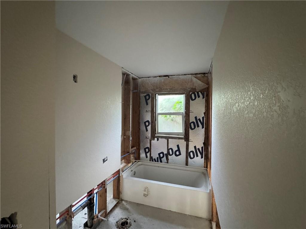 Bathroom under construction featuring a white bathtub, a window, and exposed wall studs