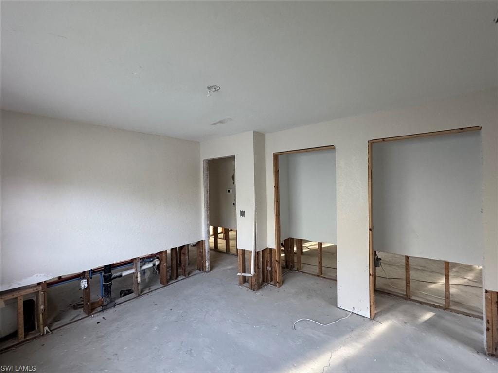 Interior space featuring exposed wall framing, unfinished concrete flooring, and ceiling-mounted light fixture rough-ins