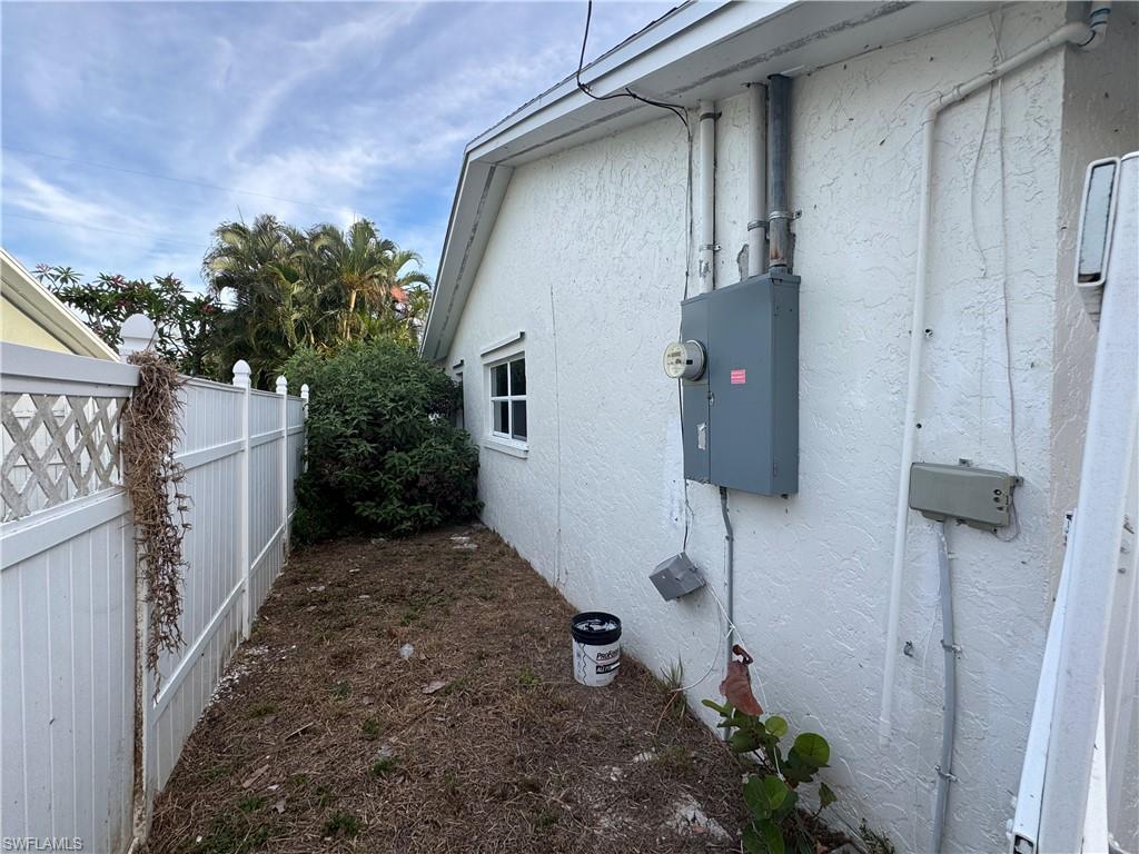 White stucco exterior featuring a side yard with a white lattice-top fence and established shrubbery