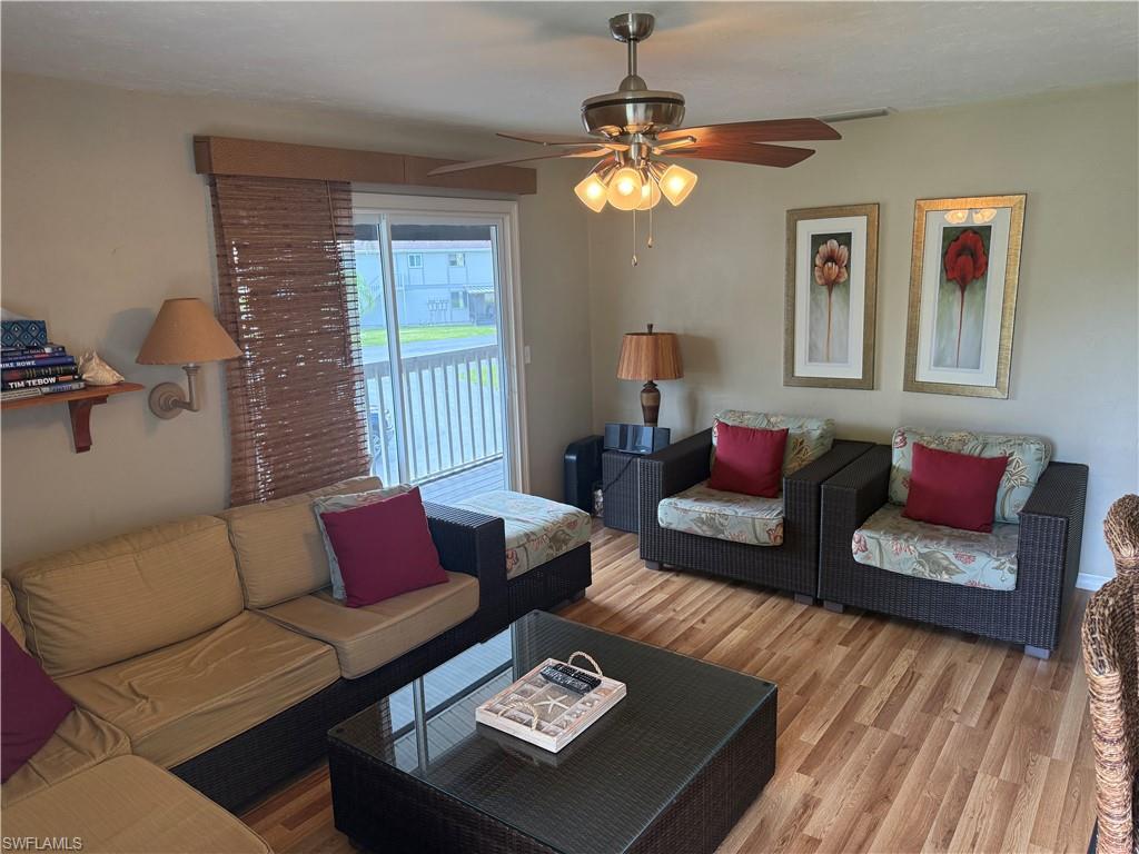 Living area featuring wood-finish flooring, a ceiling fan with integrated lighting, and a glass sliding door leading to an outdoor deck with white railings