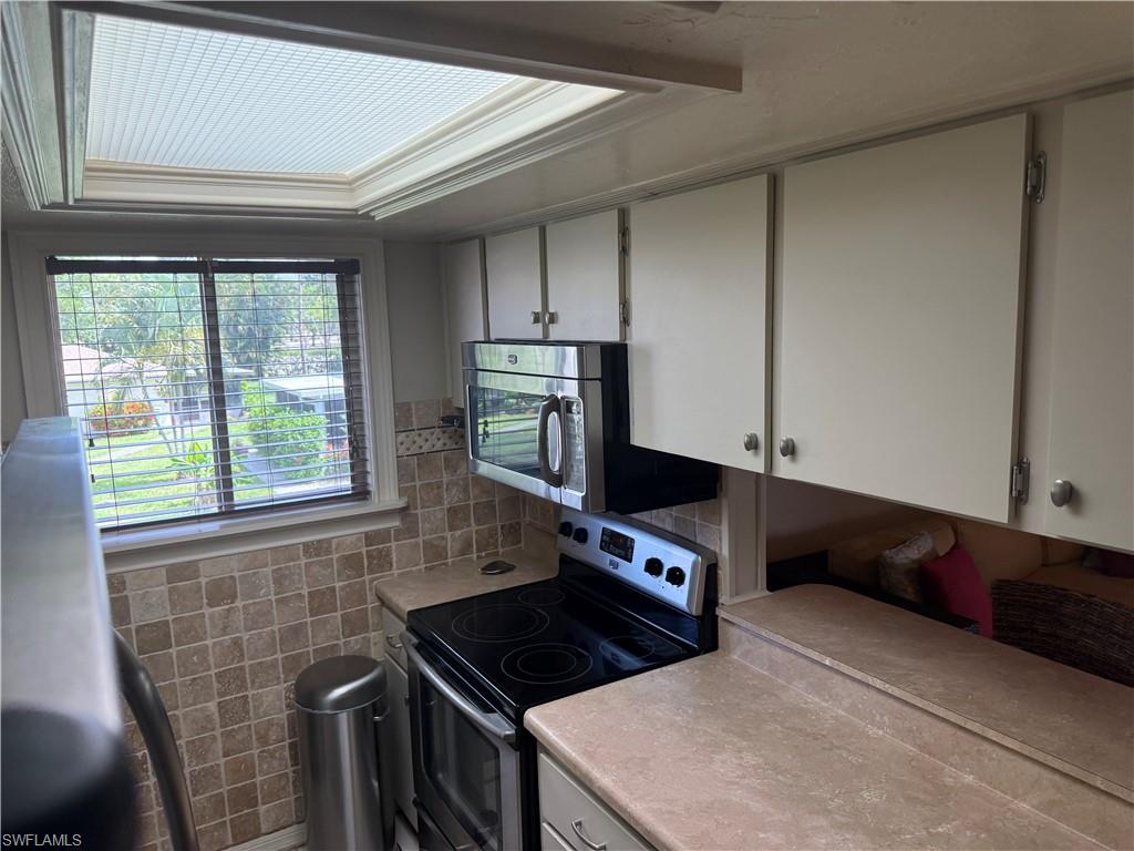 Kitchen area featuring a window with horizontal blinds, a tiled backsplash, overhead cabinetry, a built-in microwave, and an electric range