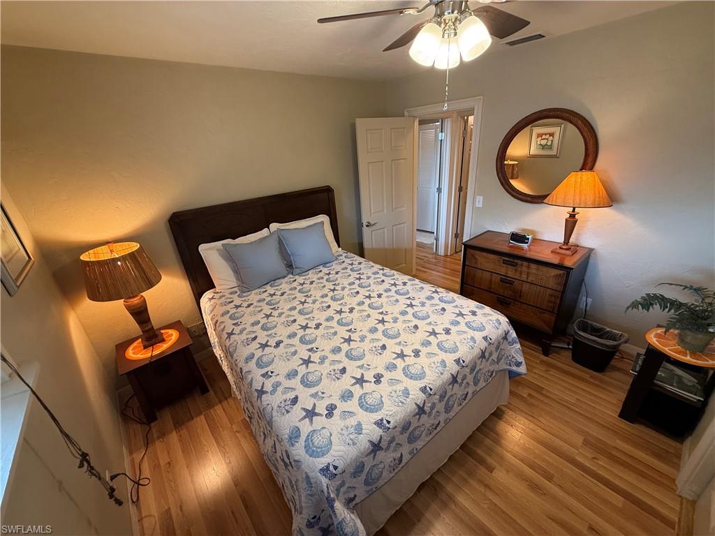 Room featuring wood-finish flooring, a ceiling fan with integrated lighting, and a paneled interior door