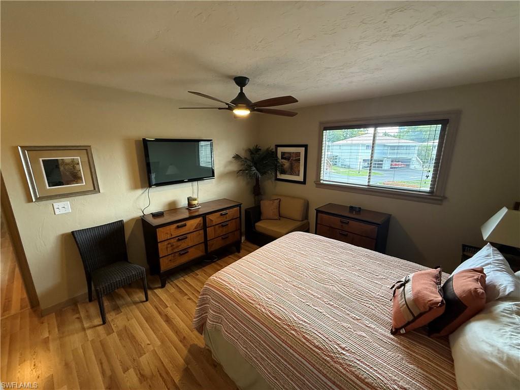 Bedroom featuring wood-finish flooring, a ceiling fan with integrated lighting, a window with horizontal blinds, and a wall-mounted flat-screen television