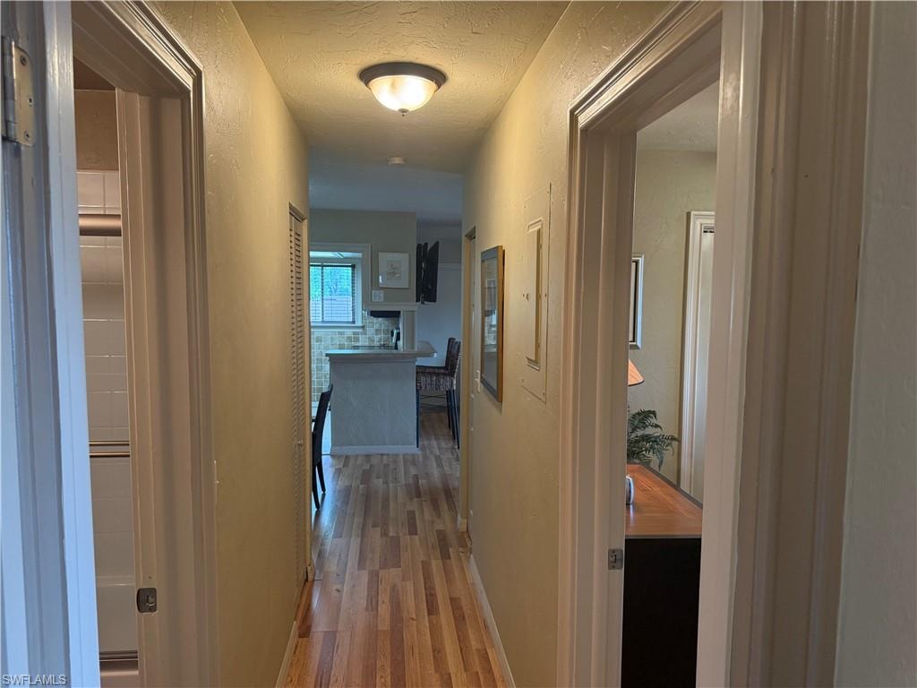 Hallway featuring wood-finish flooring, a flush-mount ceiling light, and access to additional rooms