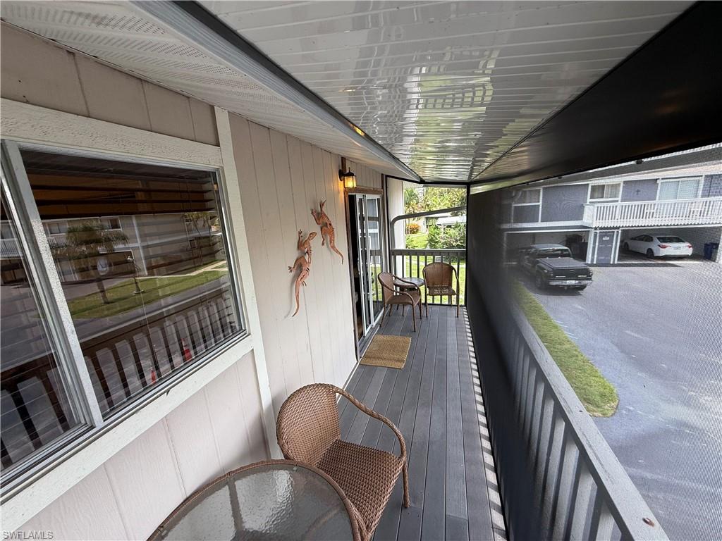 Screened balcony featuring wood-finish decking, white railings, and a sliding glass door entry