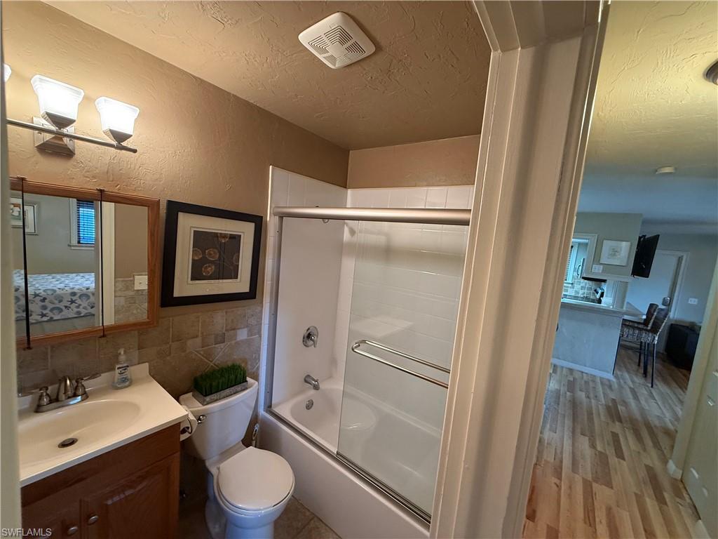 Full bathroom featuring a single vanity, tiled backsplash, and a tub/shower combination with a sliding glass door