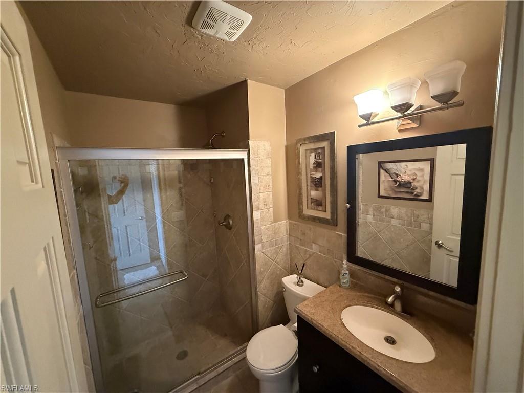 Bathroom featuring a glass-enclosed shower, tiled shower surround, vanity with an integrated sink, framed mirror, and a three-light fixture