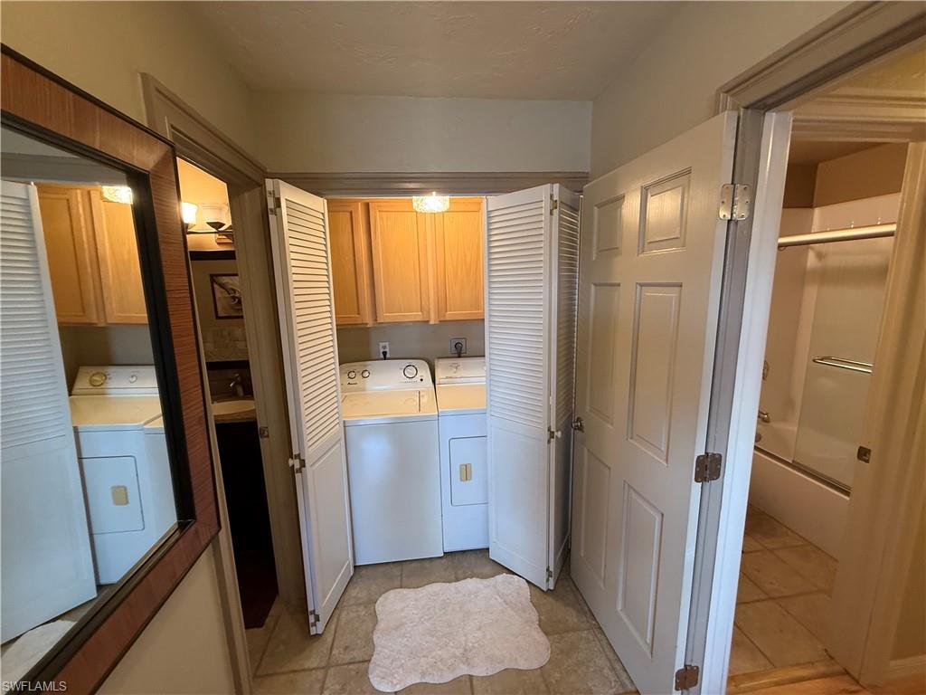 Dedicated laundry area featuring bi-fold louvered doors, overhead cabinetry, and tile flooring