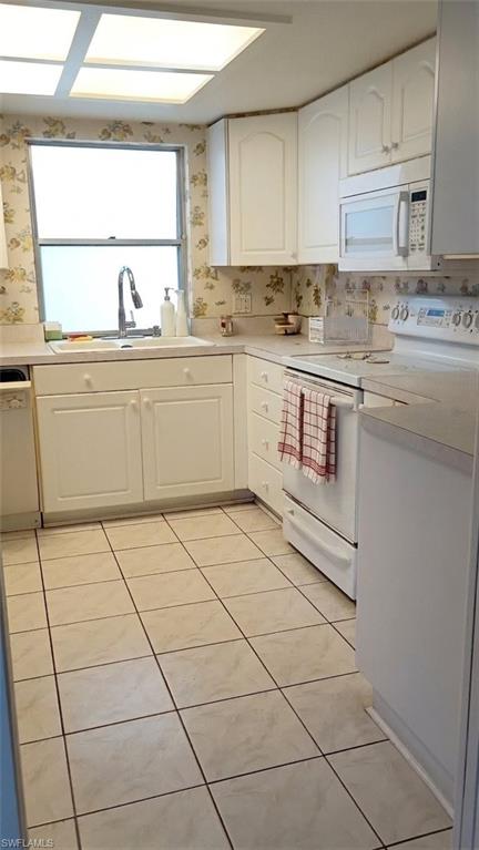 Kitchen featuring white cabinetry, tile flooring, a window above the sink, a white built-in microwave, and an electric range
