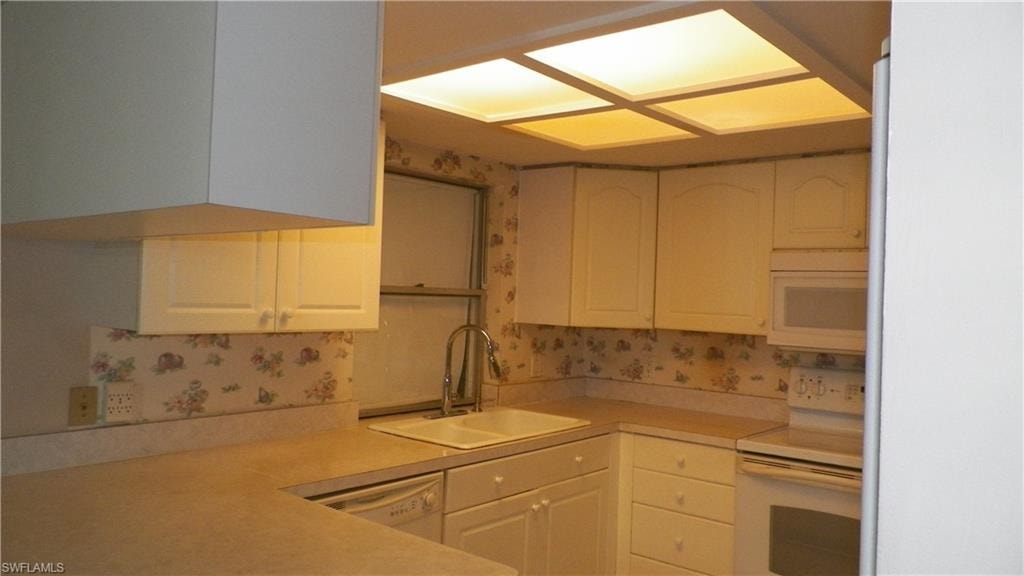Kitchen featuring white cabinetry, light-toned countertops, a double basin sink with a chrome faucet, a built-in microwave, and a white range