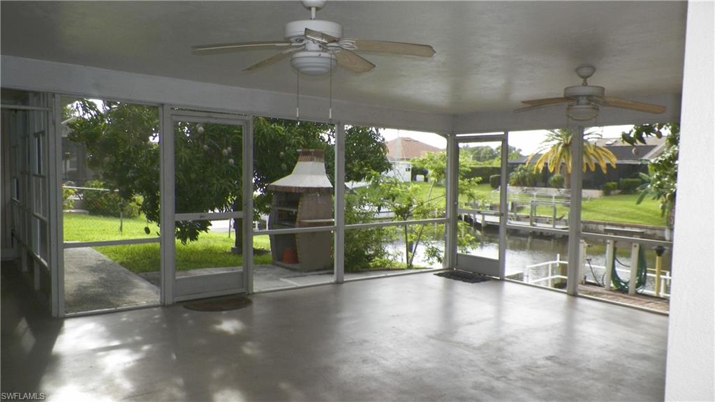 Spacious screened lanai featuring an integrated brick-clad outdoor cooking area, two ceiling fans, and concrete flooring