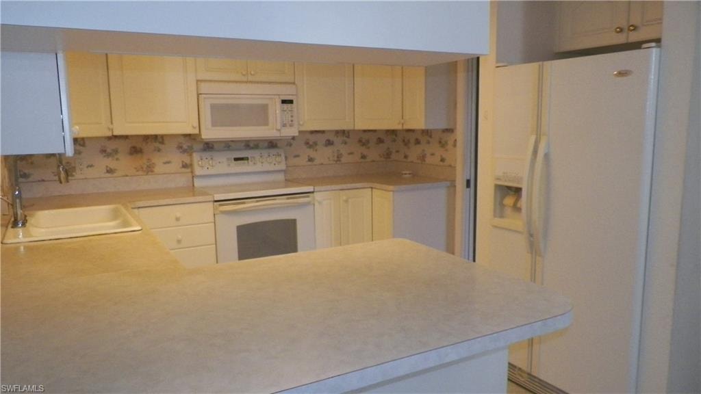Kitchen featuring white cabinetry, white range, built-in microwave, white sink, and light-toned countertops