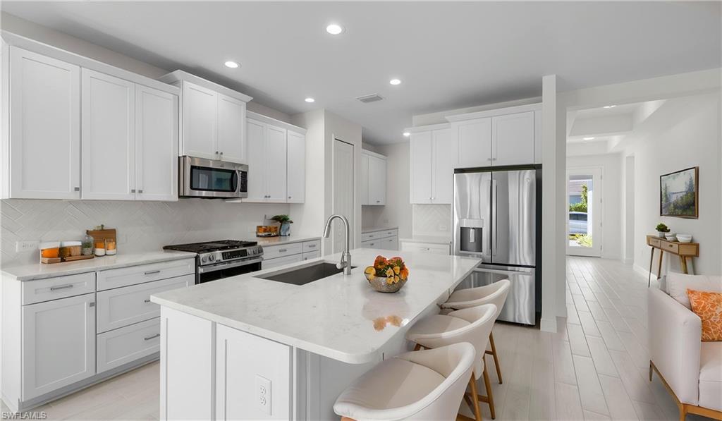 Featuring crisp white cabinetry, quartz countertops, stainless steel appliances, a gas range, oversized island seating, soft-close cabinetry, and a designer herringbone backsplash, this beautifully appointed kitchen blends style and functionality. Whether preparing a casual breakfast or hosting guests, this space serves as the centerpiece of the home