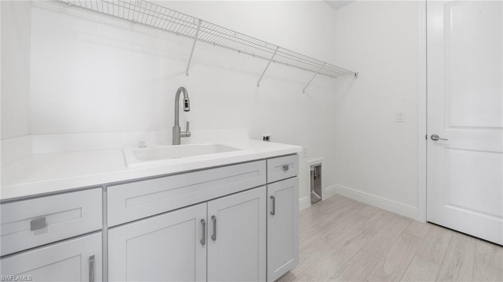 Laundry area featuring a utility sink with a modern faucet, white countertops, light gray cabinetry with brushed nickel hardware, and light wood-finish flooring