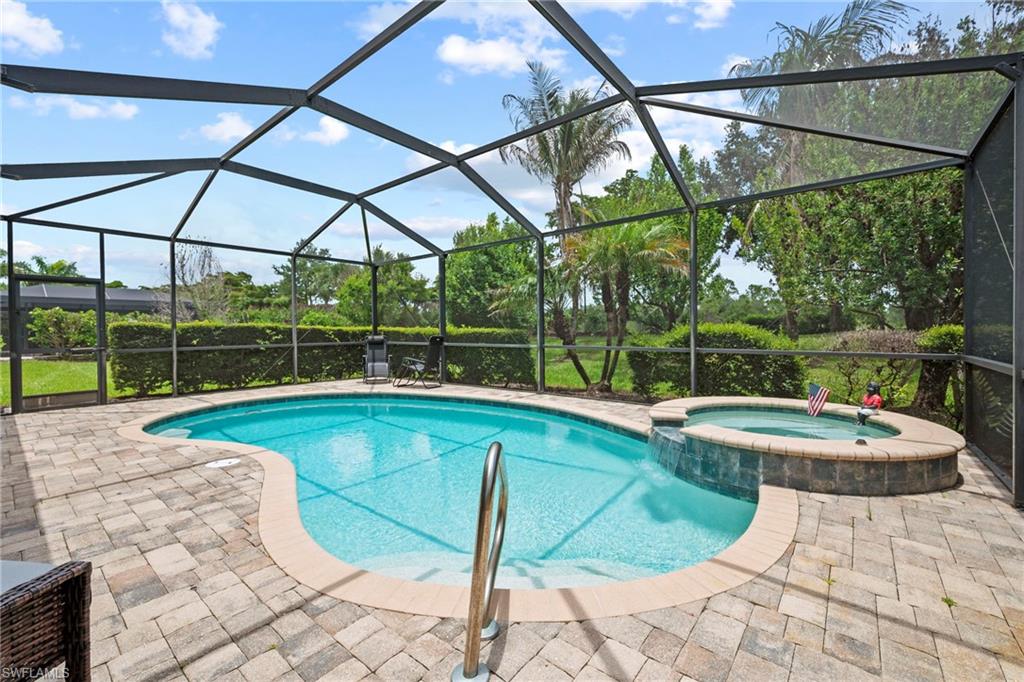 Screened-in outdoor living space featuring a freeform pool, integrated spa with a waterfall feature, and ample paver decking