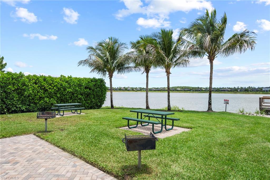 Grassy outdoor area featuring multiple picnic tables, two barbecue grills, and mature palm trees