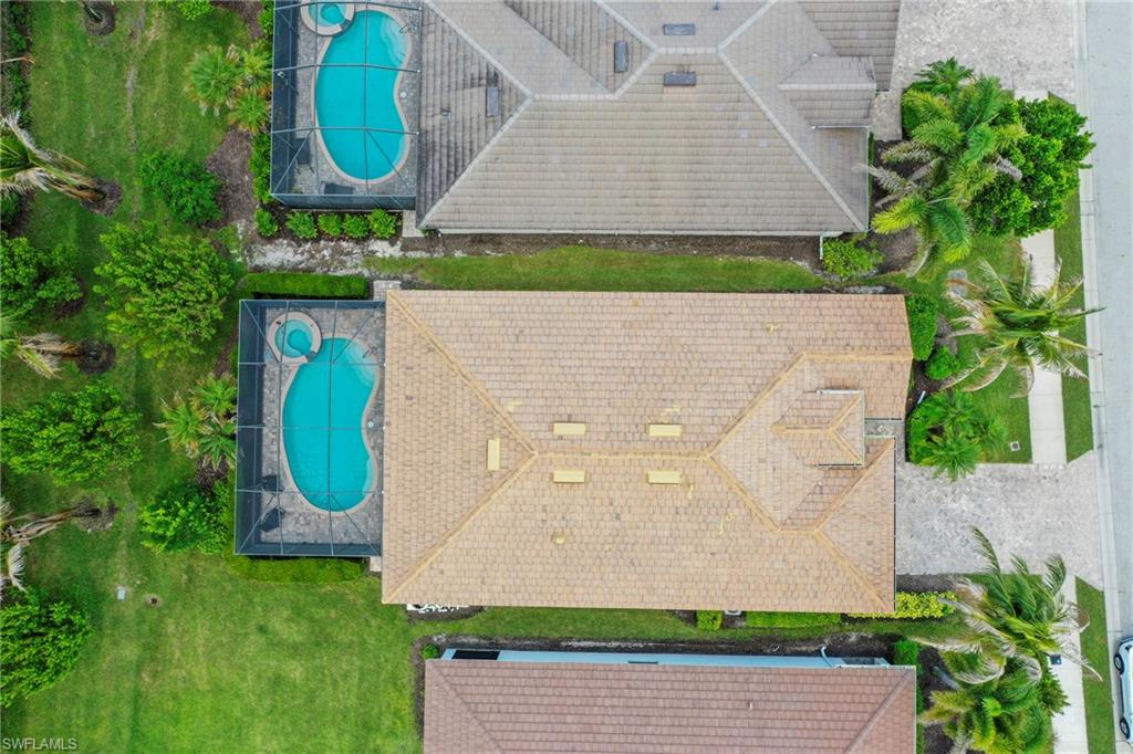 Aerial perspective showcasing a property with a light brown tile roof, mature landscaping, and an enclosed pool area featuring a kidney-shaped pool and integrated spa