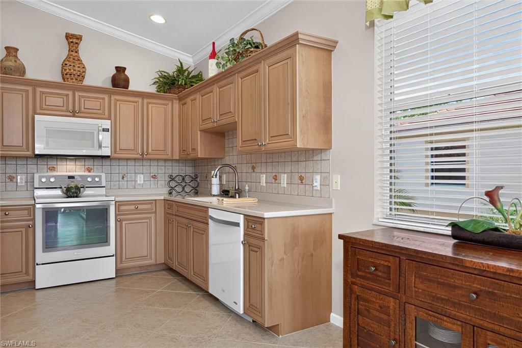 Kitchen featuring light wood cabinetry with crown molding, a tile backsplash, light-toned countertops, and integrated appliances