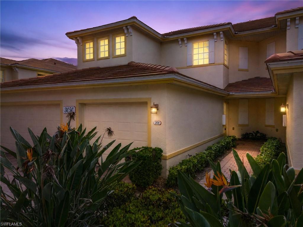 Mediterranean-style facade featuring stucco exterior, terracotta roof tiles, twin garage doors, decorative window shutters, and a brick paver pathway